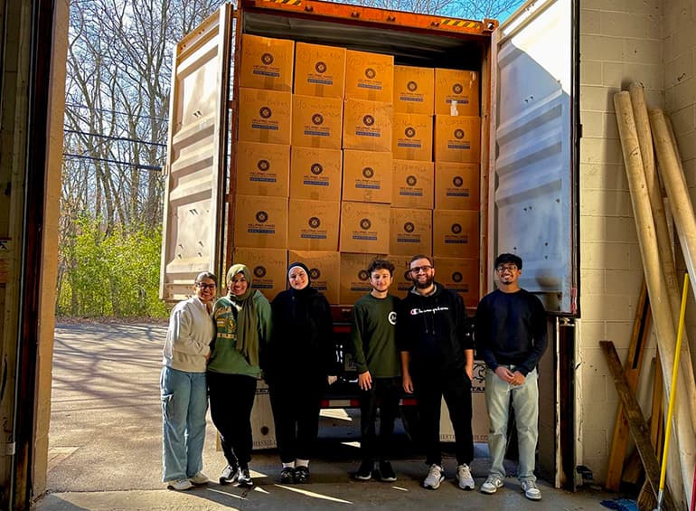 group of Muslim students standing in front of truck loaded with boxes